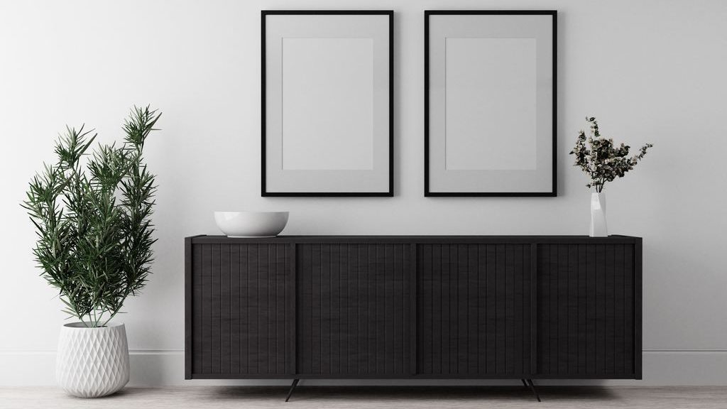 Black slatted sideboard against a white wall with two framed minimalist prints, a potted plant, and simple ceramic decor.