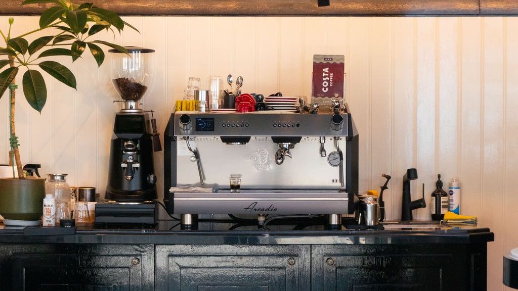 Coffee station on a black buffet cabinet with an espresso machine, grinder, glassware, and coffee accessories.