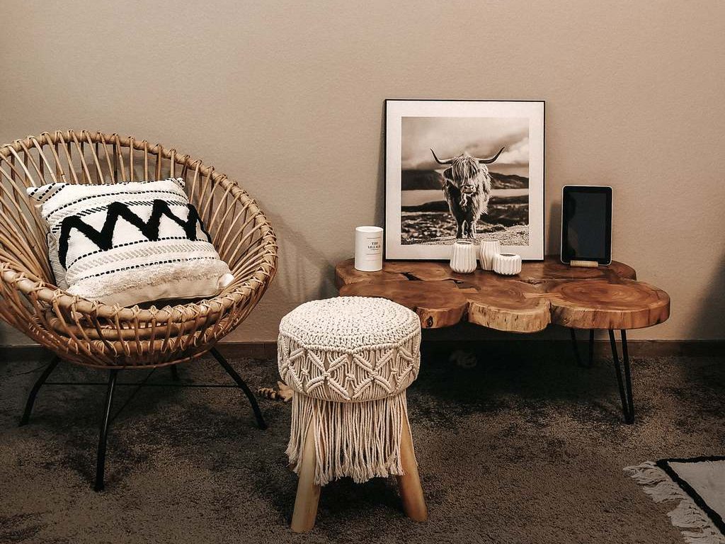 Boho decor corner with rattan chair, patterned pillow, macramé stool, natural wood table, framed wall art, and warm earthy tones.