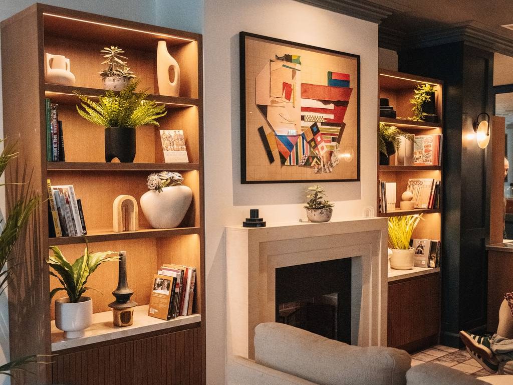 Stylish lounge with an unused fireplace, colorful wall art, built-in wood shelves, indoor plants, warm lighting, and modern seating.