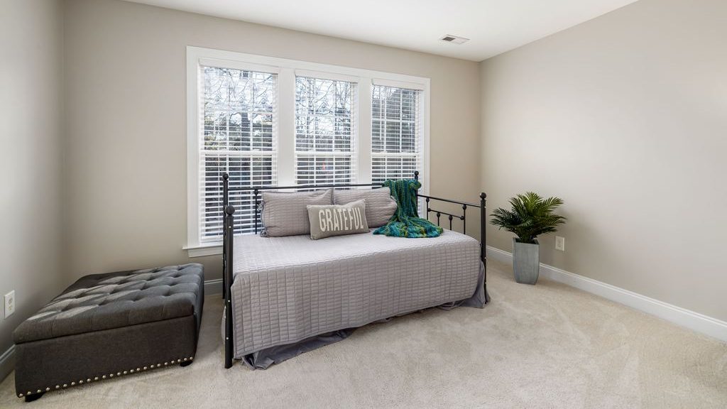 Gray daybed with black metal frame beneath a large window, styled with pillows and a teal throw in a neutral guest room.