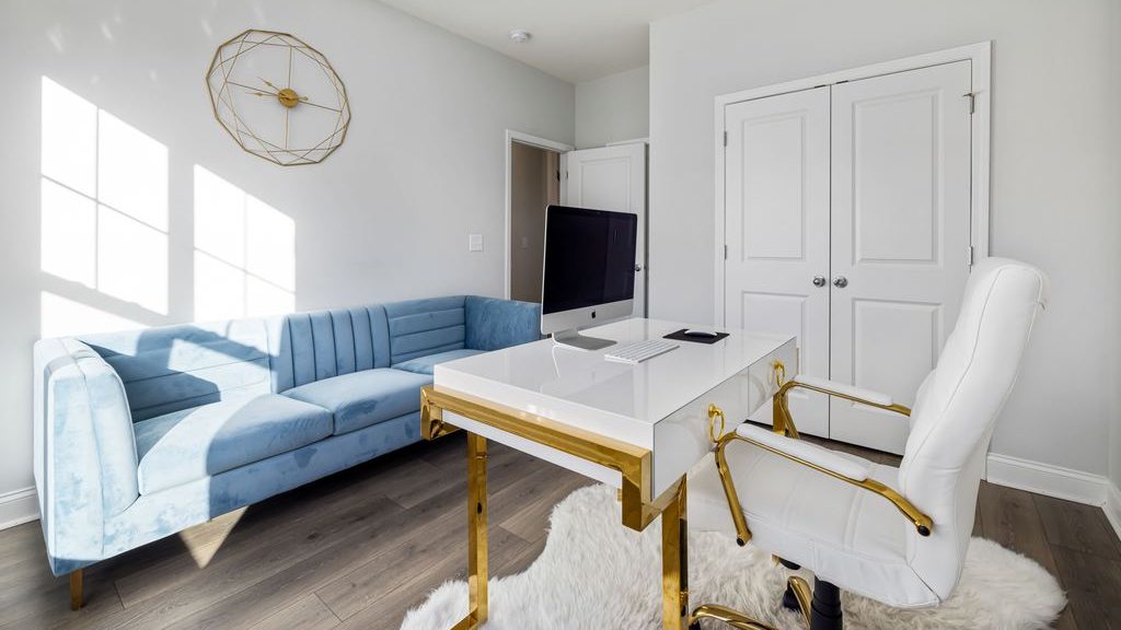Bright home office with a blue velvet sofa, white desk, computer, and white-and-gold office chair.