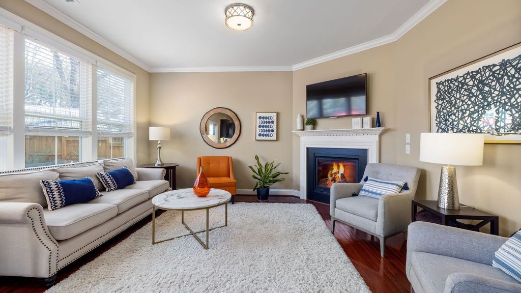 Cozy family room with a white sofa, gray armchairs, plush area rug, marble coffee table, fireplace, and layered table lamps.