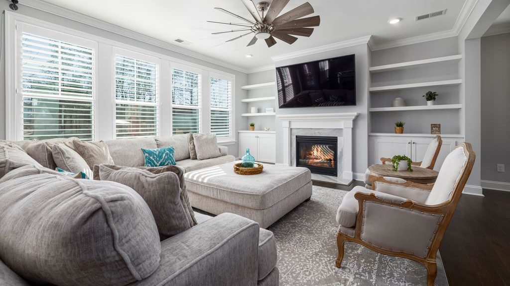 Light upholstered accent chairs arranged beside a large sectional in a bright living room with a fireplace and wall-mounted TV.