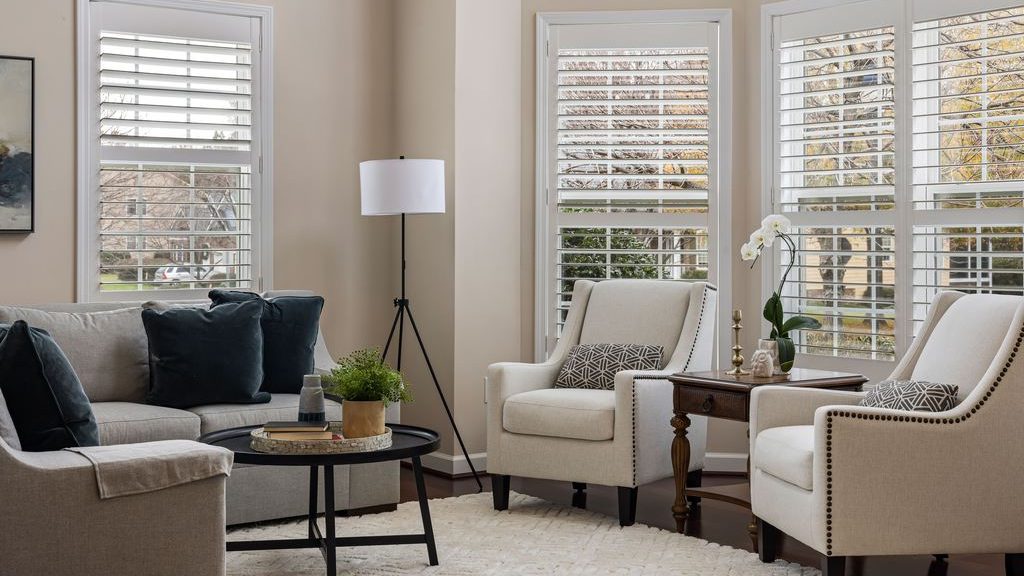 White upholstered accent chairs placed beside a gray sofa, with a small side table and floor lamp creating a bright window-side conversation area.