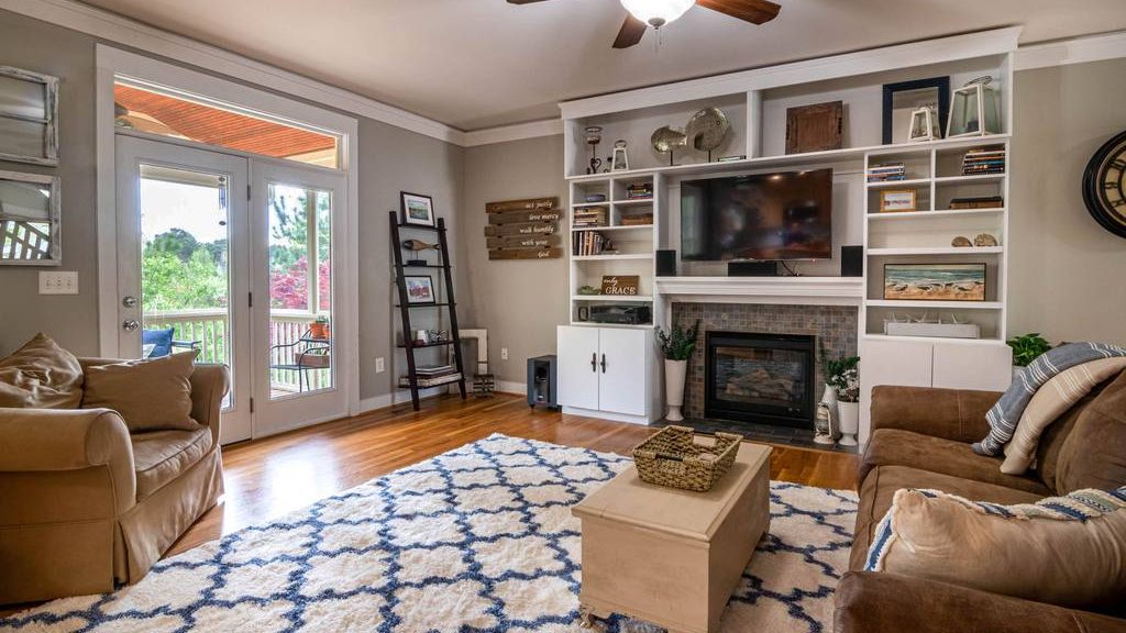 Traditional living room with brown sofas, a blue-and-white patterned rug, central storage coffee table, built-in shelving, fireplace, wall-mounted TV, and glass patio doors.