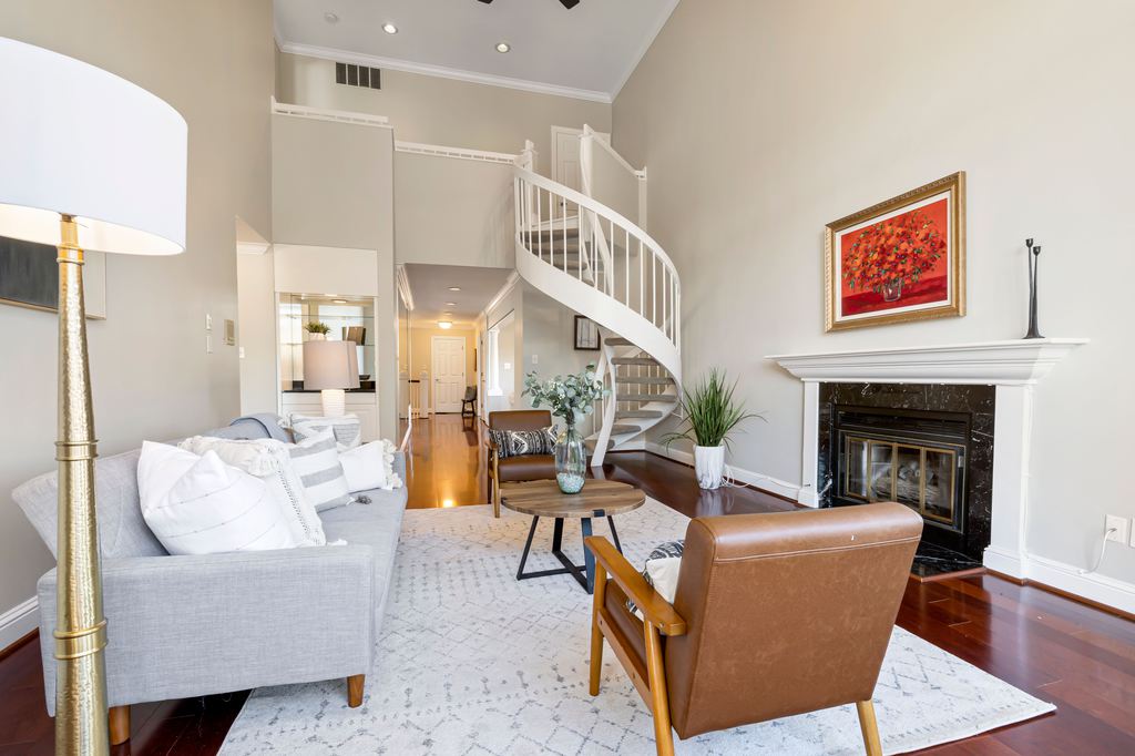 Bright rental living room with gray sofa, leather accent chairs, area rug, floor lamp, fireplace, and tall neutral walls.