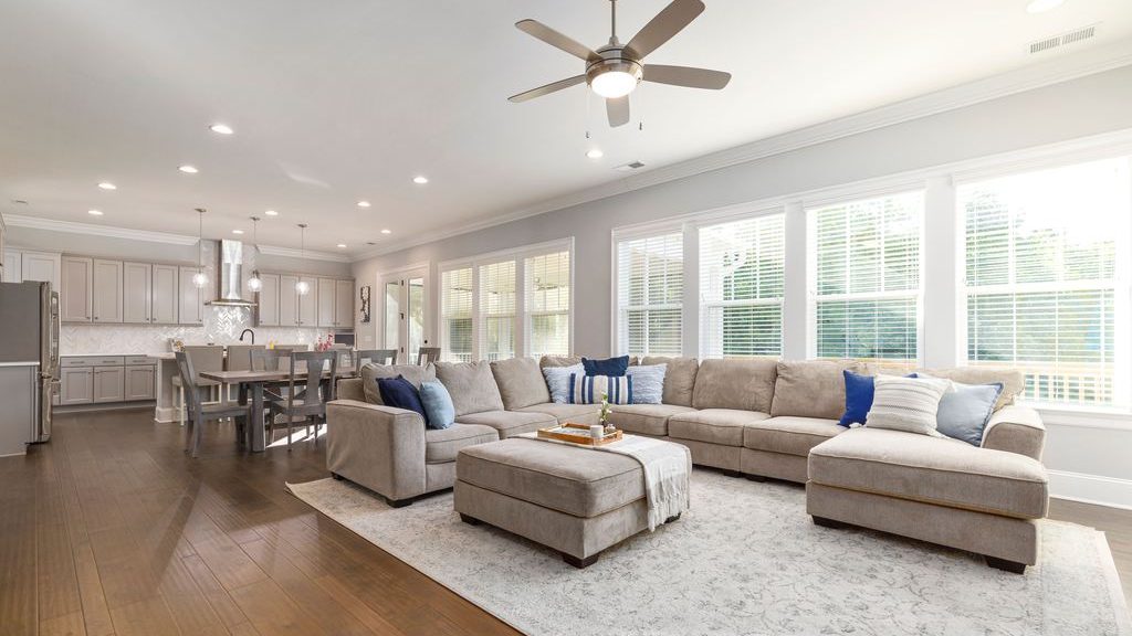 Open-concept living room with a large beige sectional, ottoman coffee table, and adjacent kitchen and dining area.