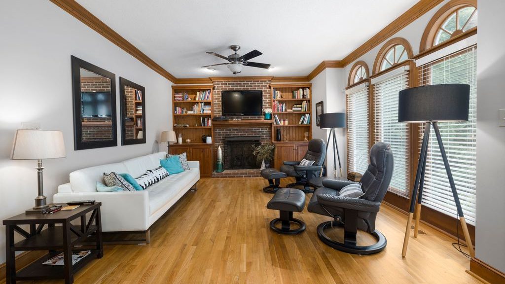 Two black leather swivel recliners with ottomans facing a white sofa in a bright living room with a fireplace and TV.