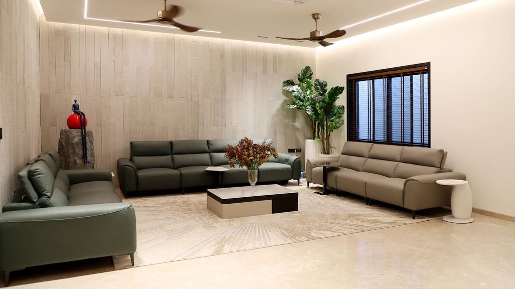 Modern living room with three leather sofas, a central coffee table, decorative plants, ceiling fans, and warm recessed lighting.