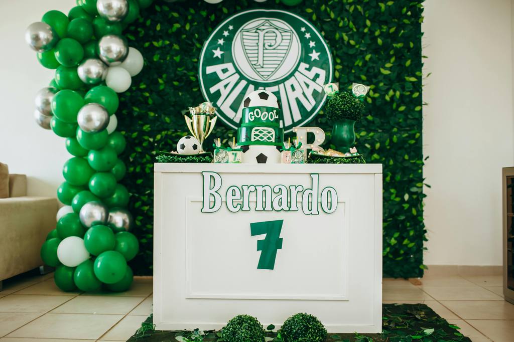 Green soccer-themed party dessert table with balloon garland, leafy backdrop, Palmeiras logo, soccer cake, trophy decor, and personalized Bernardo sign.