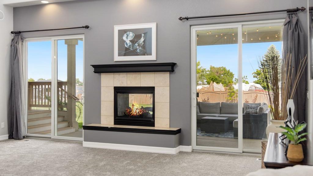 Modern living room with a gray fireplace wall, lit fireplace, framed artwork, patio doors, recessed lighting, and neutral decor.