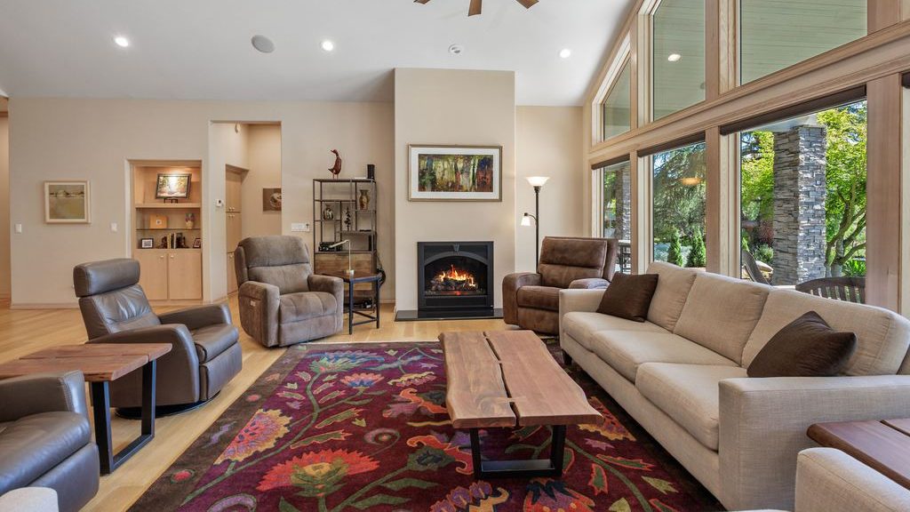 Living room with a cream sofa, three recliners, a fireplace, large windows, a wood coffee table, and a colorful floral area rug.
