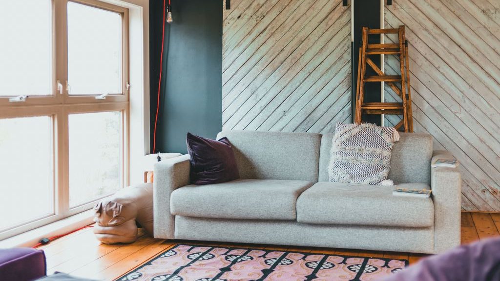 Light gray two-seat sofa with textured pillows in a bright living room with large windows, a patterned rug, and sliding barn doors.