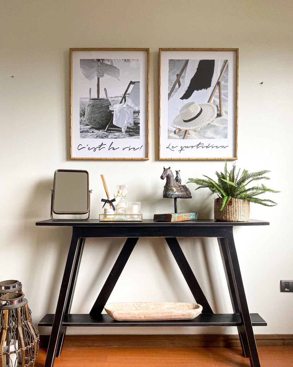 Black console table styled with a tabletop mirror, tray, horse figurine, potted fern, and framed artwork above.