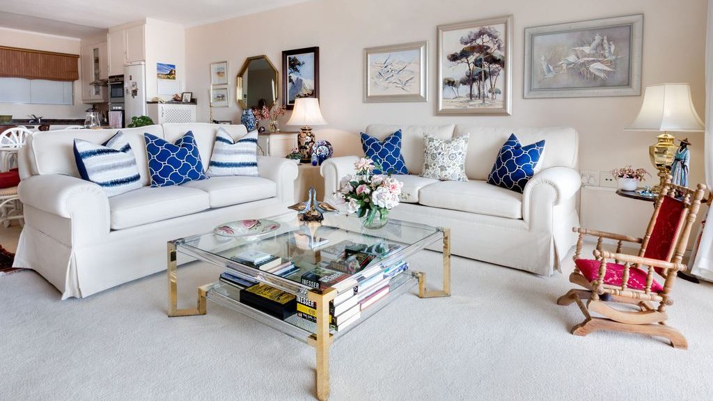 Traditional living room with two white sofas, blue patterned pillows, a glass coffee table, and a wooden rocking chair.
