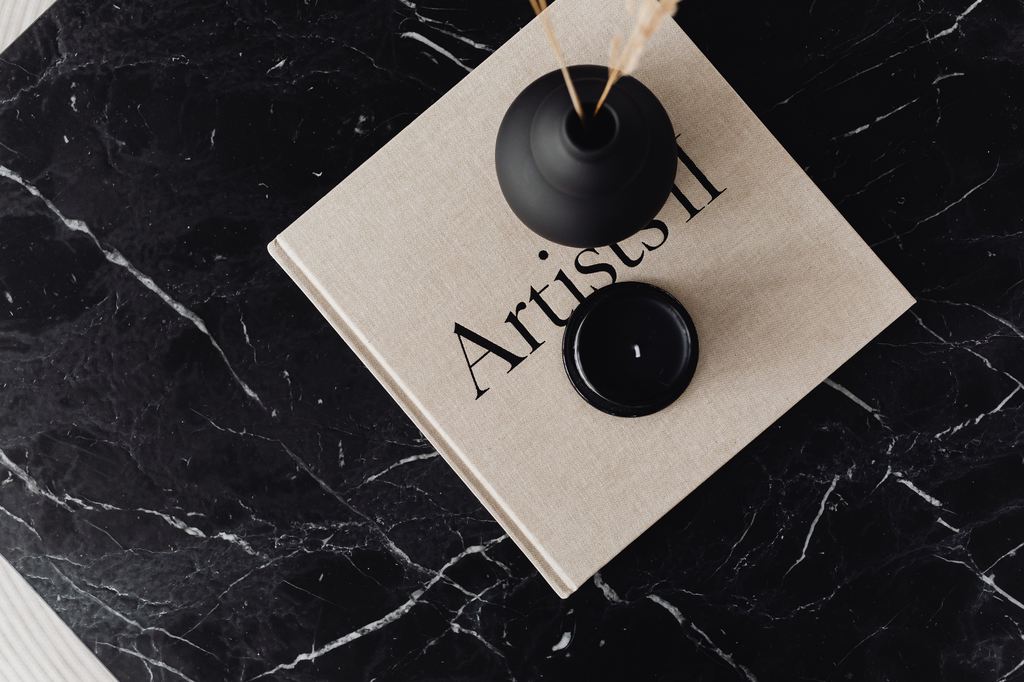Black marble coffee table styled with a beige art book, matte black vase with dried stems, and a black candle.