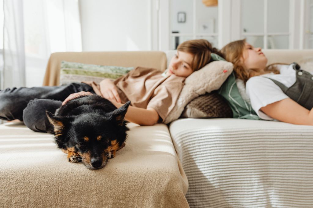 Two children and a small black dog resting on a light-colored fabric sectional sofa.