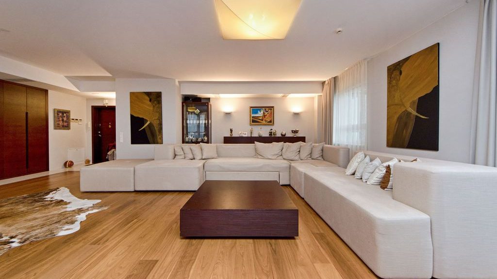 Spacious living room with a large cream U-shaped sectional sofa, dark wood coffee table, abstract wall art, and warm wood flooring.