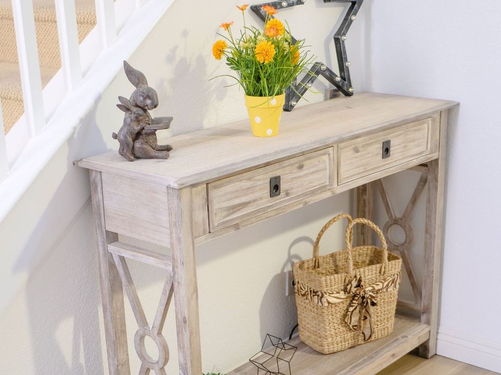 Wood console table with drawers and a lower shelf, styled with flowers, a star-shaped mirror, and a storage basket beneath a staircase.