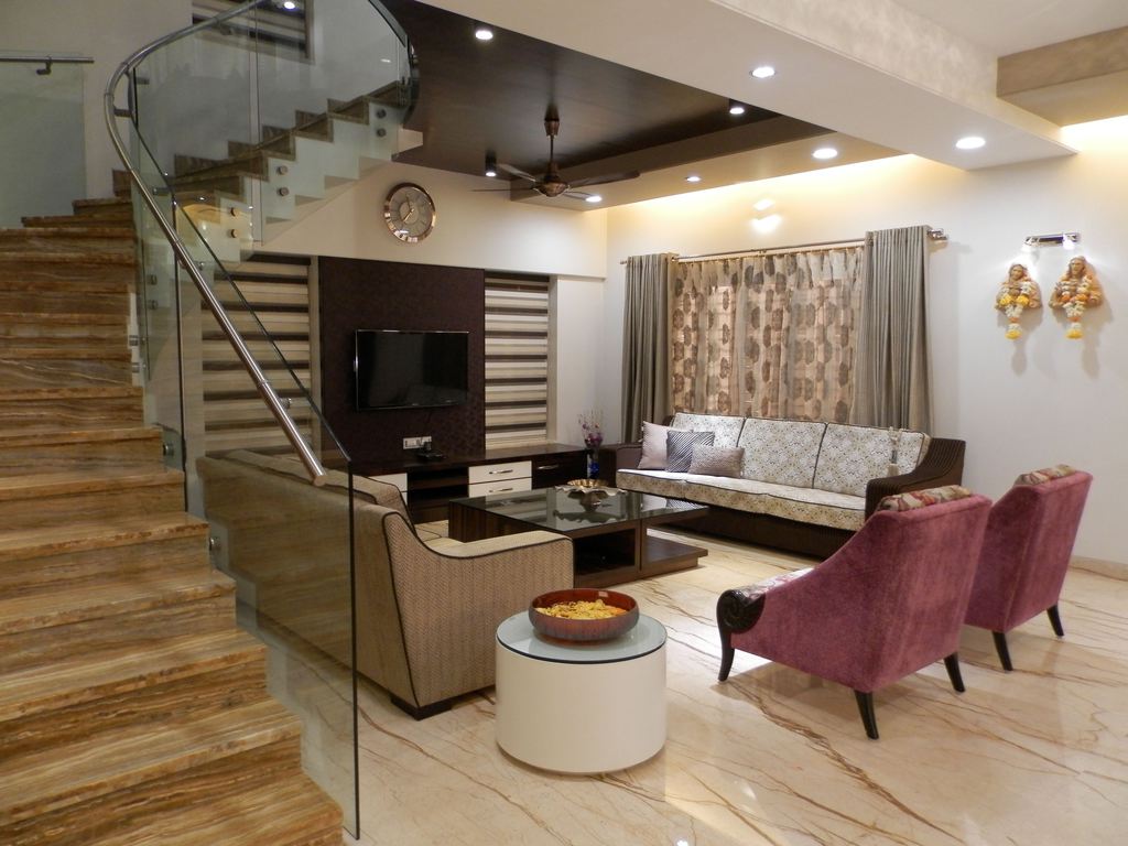 Modern living room with staircase, TV wall, patterned sofa, glass coffee table, and pink accent chairs creating an asymmetrical layout.
