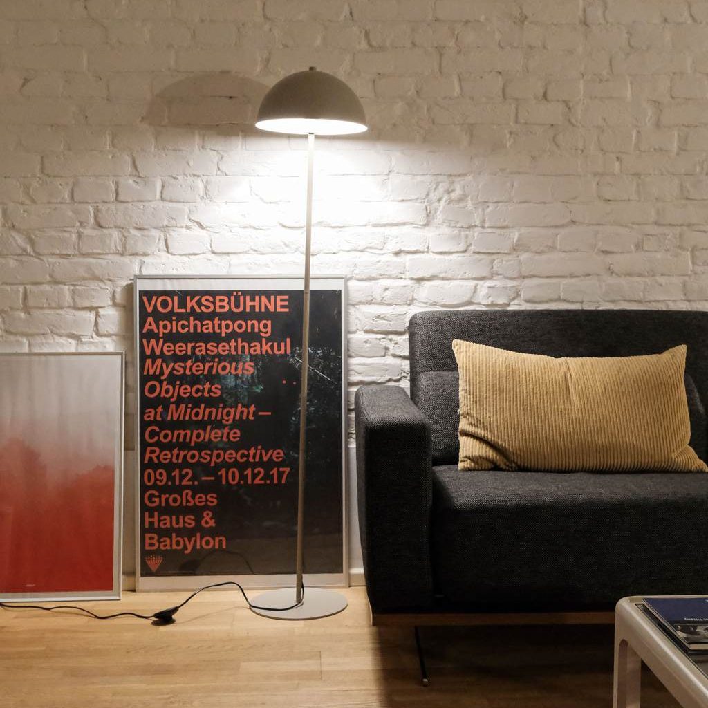 a floor lamp near a black sofa with a yellow cushion and a glass coffee table in a minimalist living room