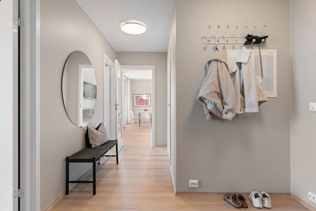 Minimalist apartment hallway with wall hooks, entryway bench, mirror, and wood flooring, showing a practical entryway landing zone for daily essentials.