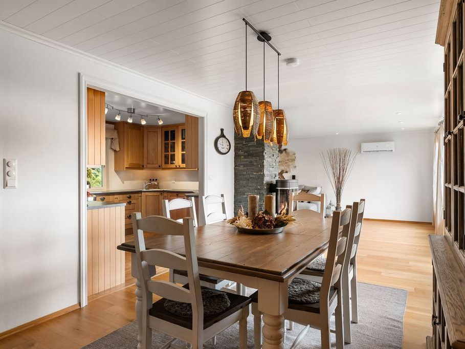 Rustic Scandinavian dining room with a warm wood table, white chairs, natural wood kitchen, pendant lighting, and a bright open living area.