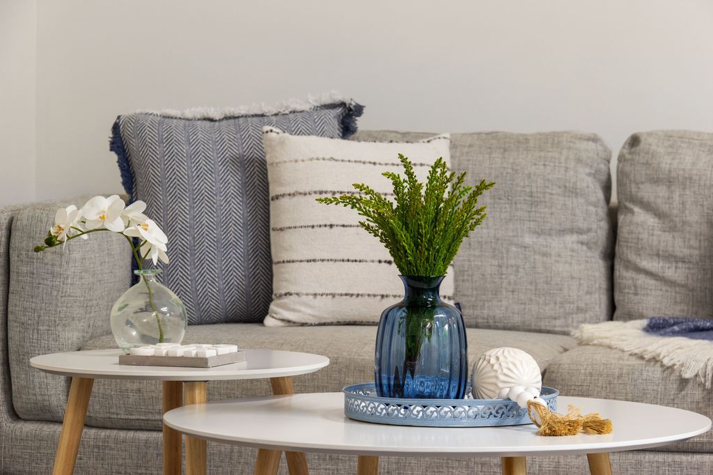 Gray living room with nested white coffee tables styled with blue glass vases, fresh greenery, orchids, and a decorative tray.