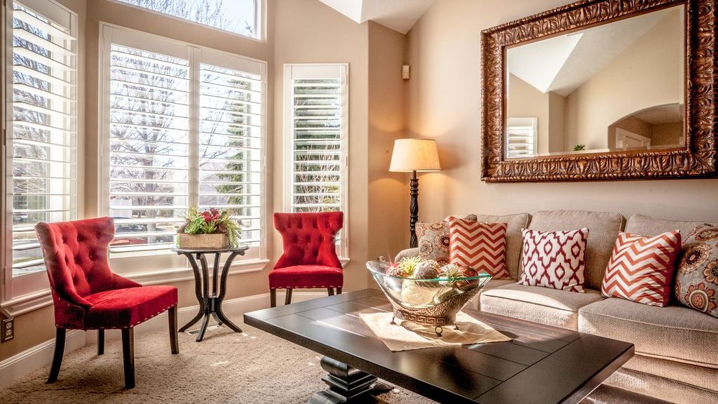 Two red accent chairs paired with a neutral sofa and dark coffee table in a bright living room with large windows.