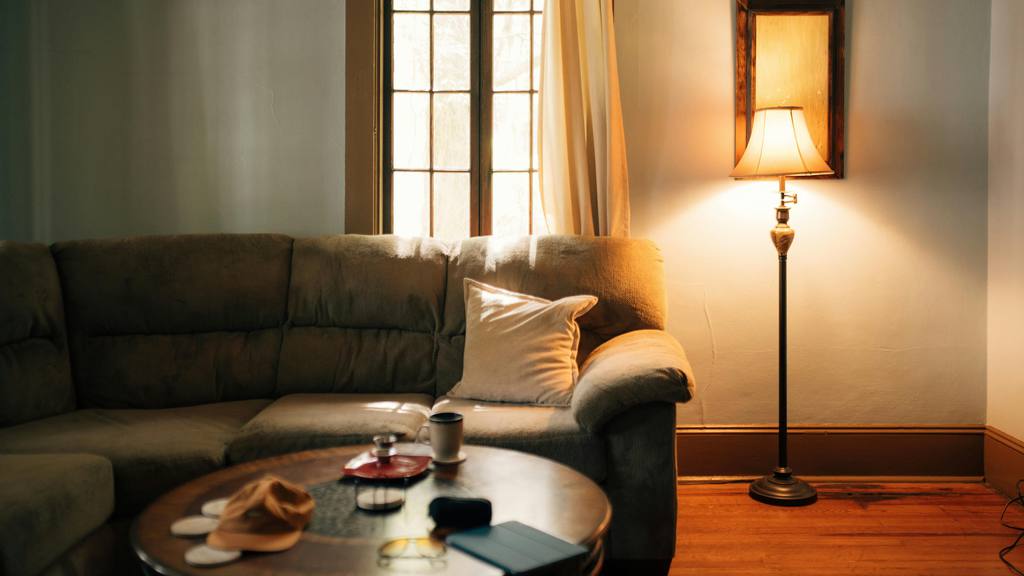 a floor lamp with warm light near a sofa with a cushion and a round wood coffee table in a dark and minimalist living room
