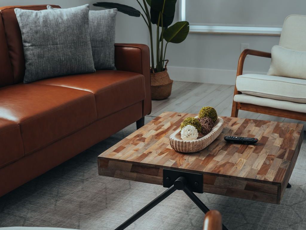 a brown leather sofa with grey cushions near a beige accent chair, a rectangular wood coffee table and a plant