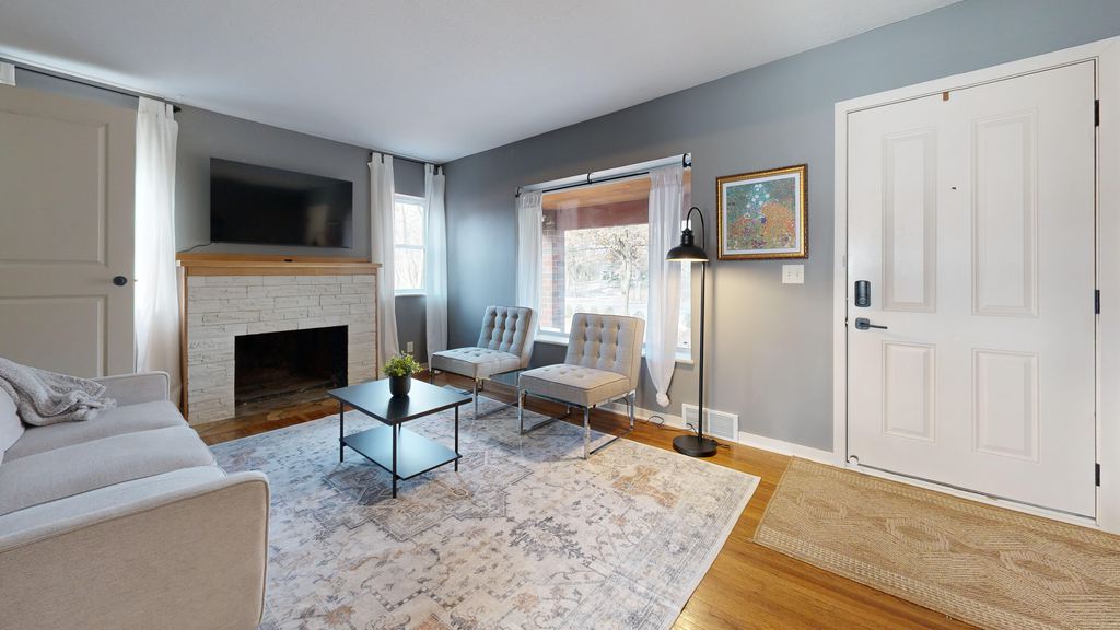 Square living room with a sofa, fireplace TV wall, two accent chairs, coffee table, and a clear entryway.