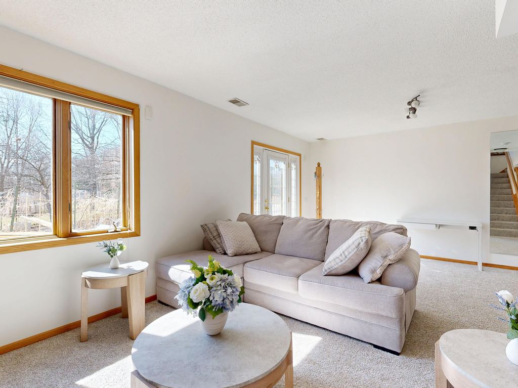 Bright living room with a beige sofa, round coffee table, side tables, and large windows overlooking a backyard.