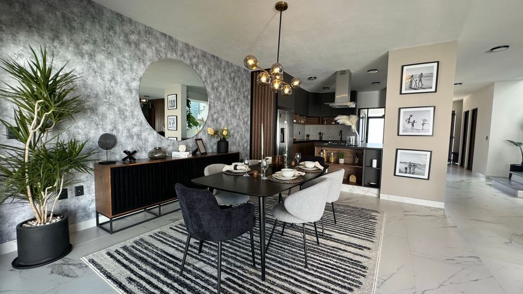 Modern dining room with a black sideboard, round wall mirror, large plant, and a set dining table in an open-concept space.