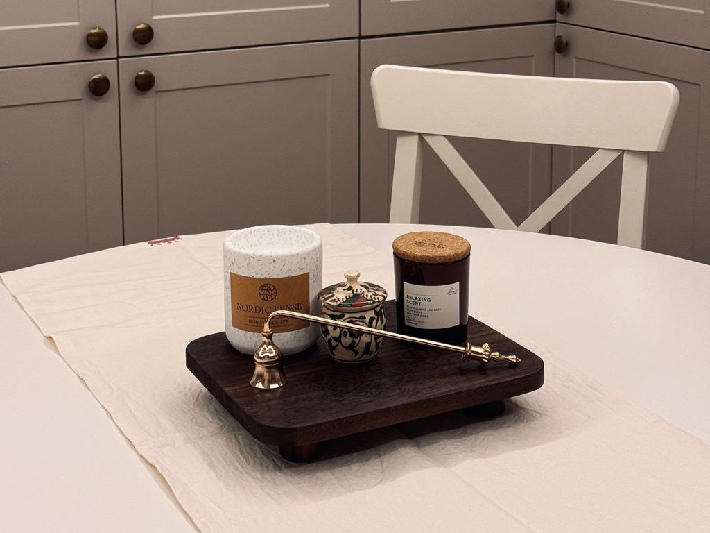 White round dining table with a linen runner and a compact wooden tray holding candles and decorative jars.