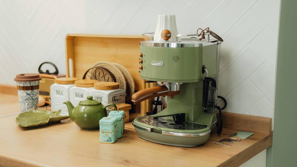 Green espresso machine on a wooden kitchen counter with tea, sugar, coffee canisters, teapot, and warm home coffee bar decor.