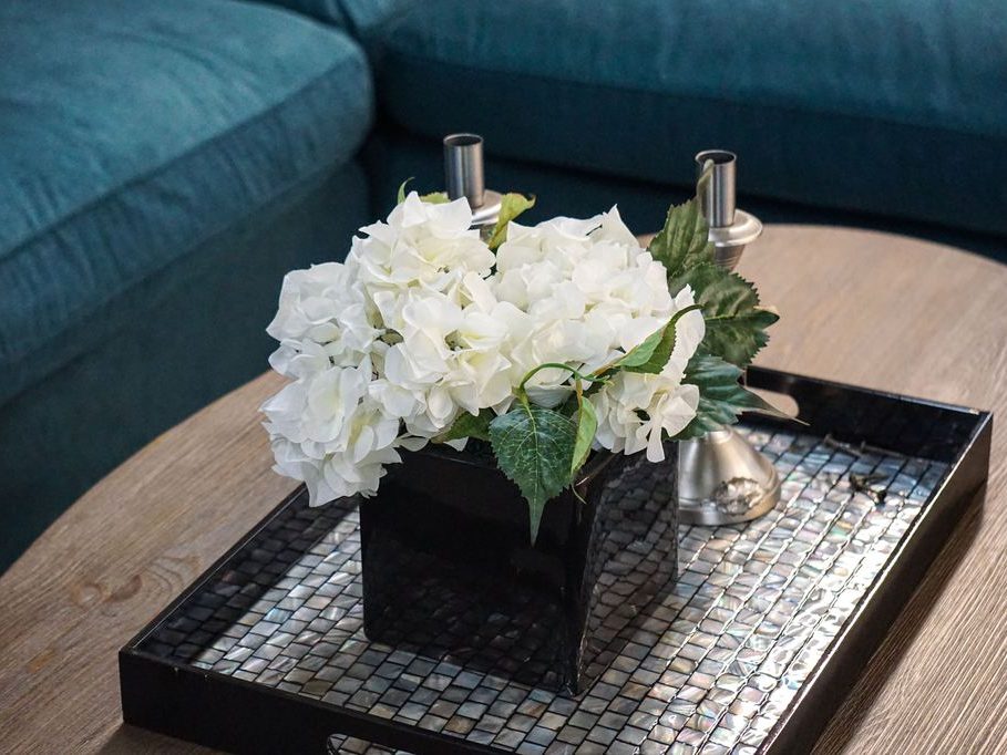 A modern elegant coffee table tray setup with a black decorative tray, white flowers, and silver candle holders on a wood coffee table.