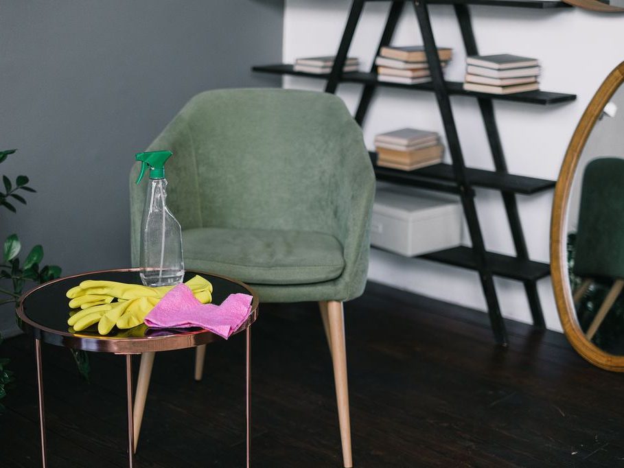 Cleaning supplies on a round side table beside a green armchair in a modern living room.