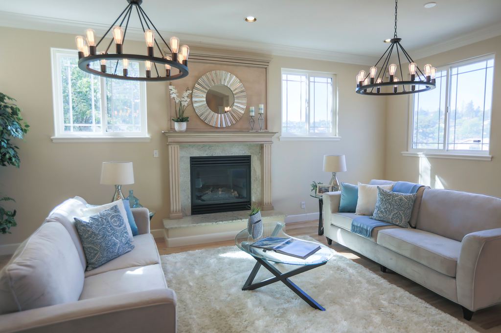 two beige sofas in opposite with blue cushions near glass side tables, a glass coffee table and a fireplace