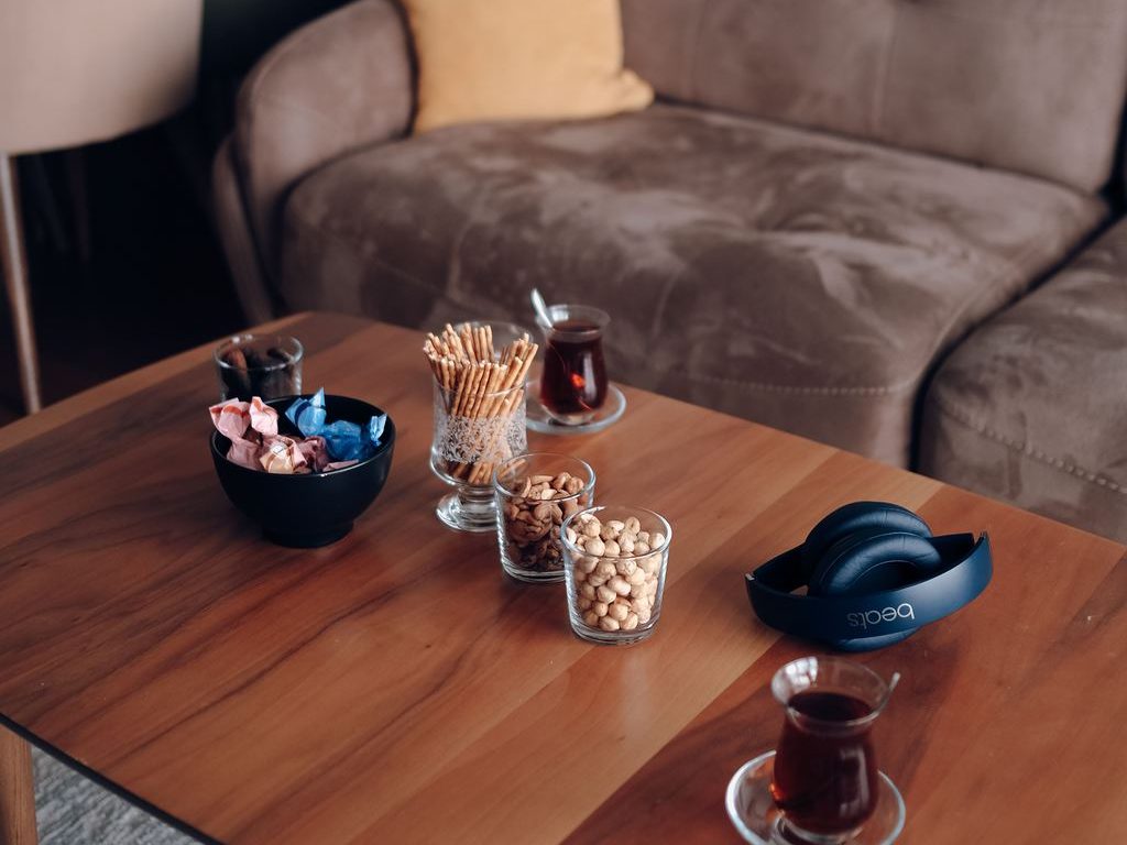 Wooden coffee table set with tea, snack bowls, breadsticks, and headphones in front of a brown sofa for a relaxed watch party.