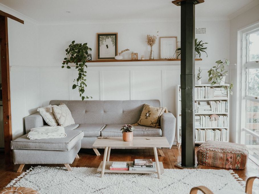 Scandinavian-style living room with a gray sectional sofa, light wood coffee table, white textured rug, indoor plants, and warm natural accents.
