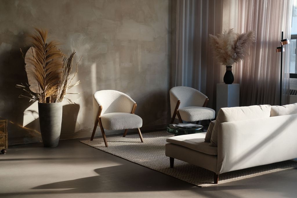 Cream boucle accent chairs and a light sofa arranged around a low coffee table in a sunlit modern living room.