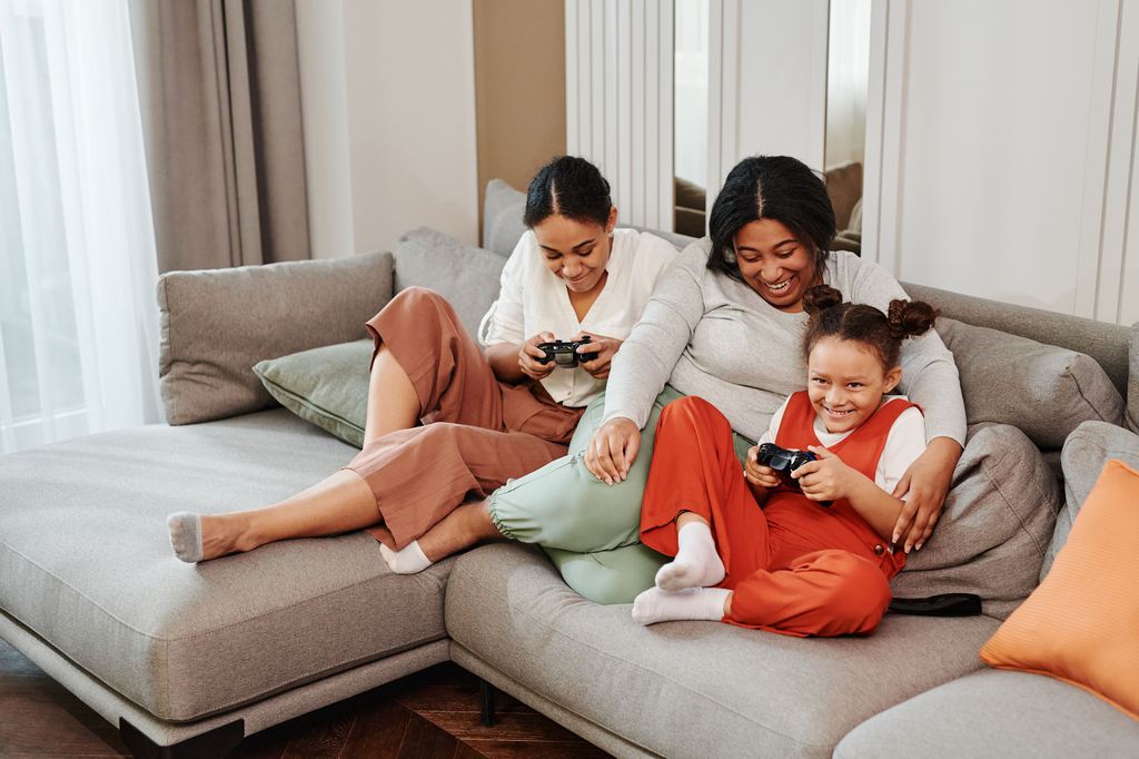 Family playing video games together on a large gray sectional sofa in a bright living room