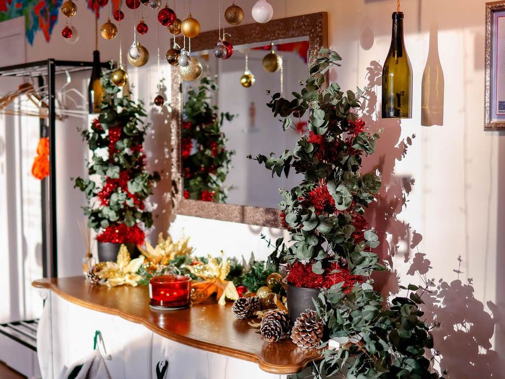 Christmas buffet table decorated with garland, red ornaments, candles, pinecones, and stockings beneath a wall mirror.