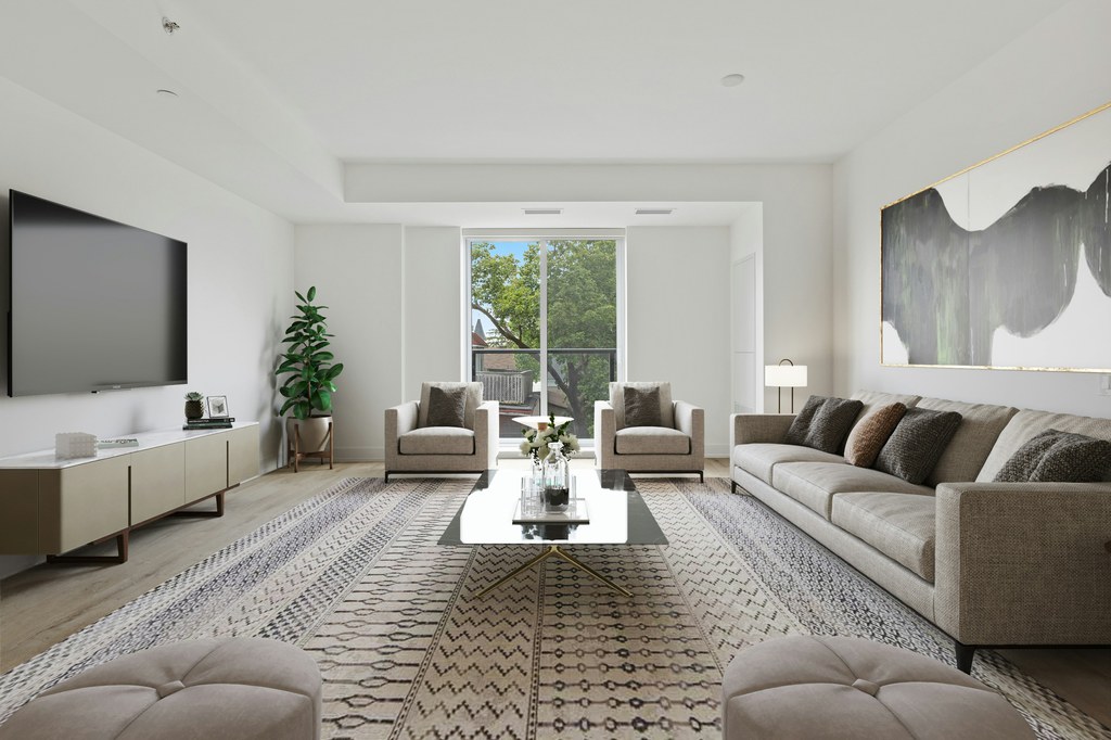 Modern living room with beige sofa, accent chairs, wall-mounted TV, low media console, and large patterned area rug anchoring the seating area.