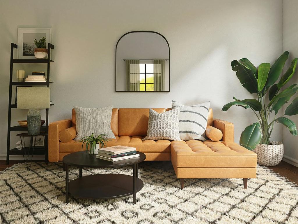 Warm living room with tan chaise sofa, round coffee table, patterned rug, arched mirror, ladder shelf, and large indoor plant.