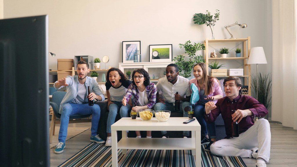 A group of friends watching a soccer match in a living room, with snacks and drinks on a white coffee table.