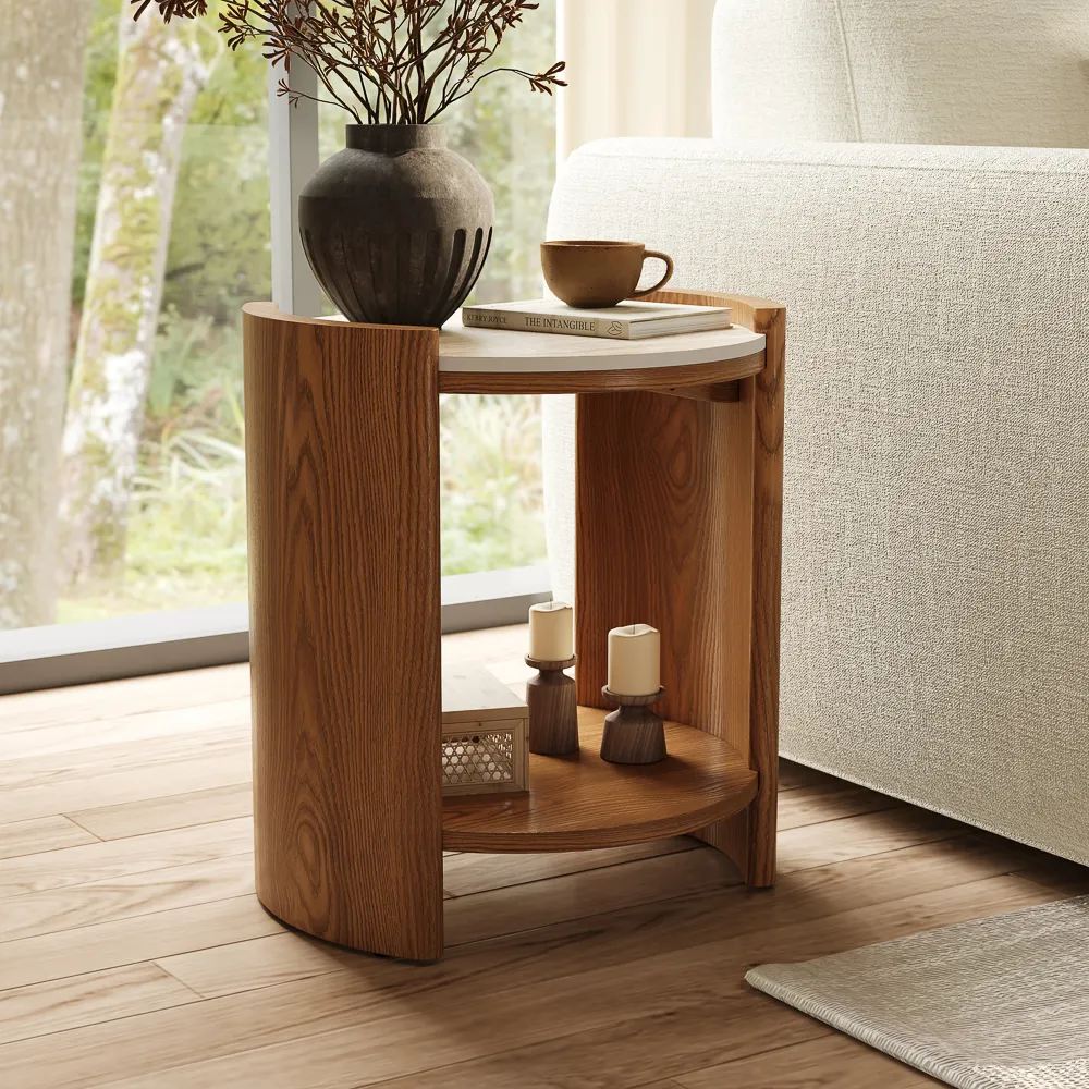 a wood side table with a tall plant, a cup on a book, two candles and stuff near a beige sofa in a bright living room