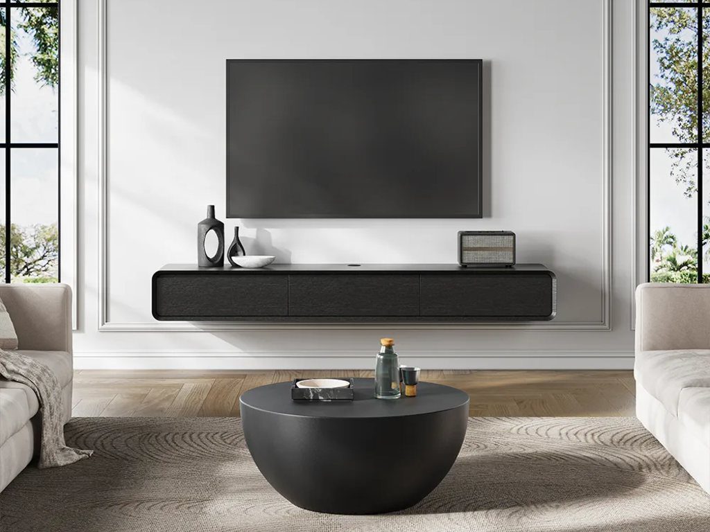 a black floating media console with a radio and some decorations below a wall-mounted tv in a minimalist living room with two white sofas and a round coffee table